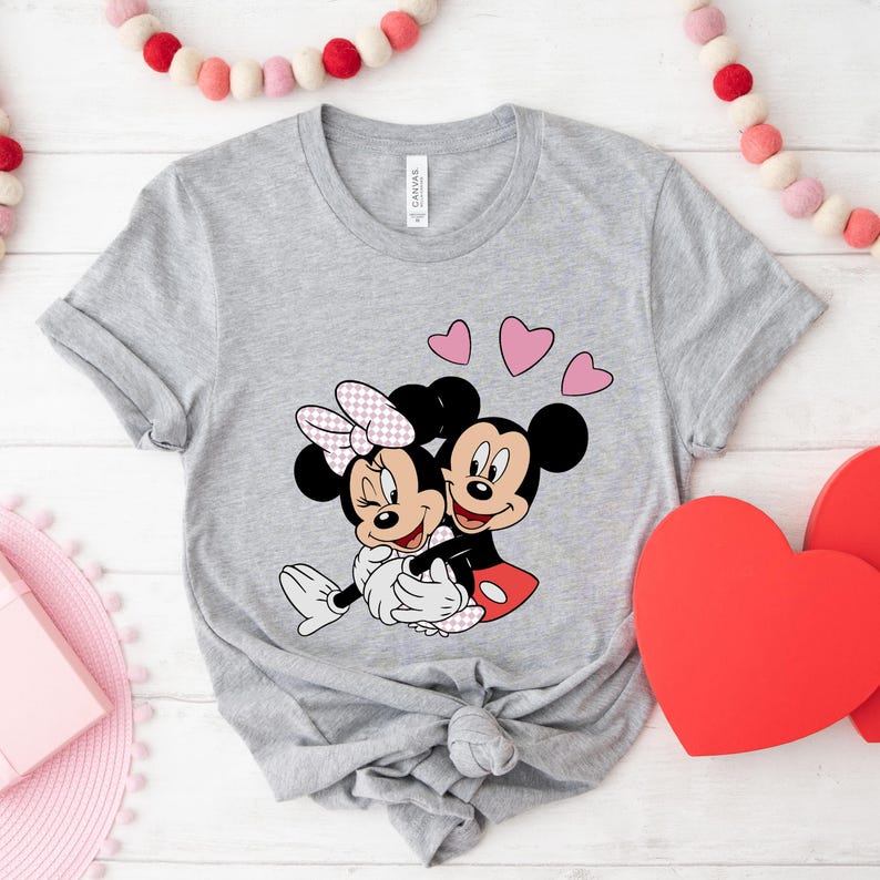 May include: A gray t-shirt with a graphic of Mickey Mouse and Minnie Mouse hugging.  There are three pink hearts above them.