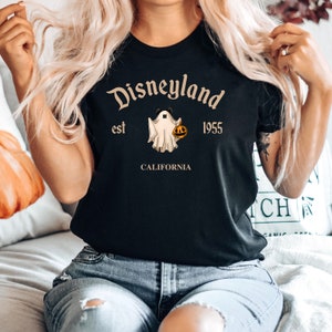 Puede incluir: Camiseta negra con un fantasma blanco que sostiene una calabaza y el texto "Disneyland est 1955 California" en marr&oacute;n.
