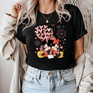 May include: Black t-shirt with a pink and red graphic of Mickey Mouse and Minnie Mouse in front of a pink castle with pink hearts and fireworks. The text "Save the Date" is visible on the graphic.