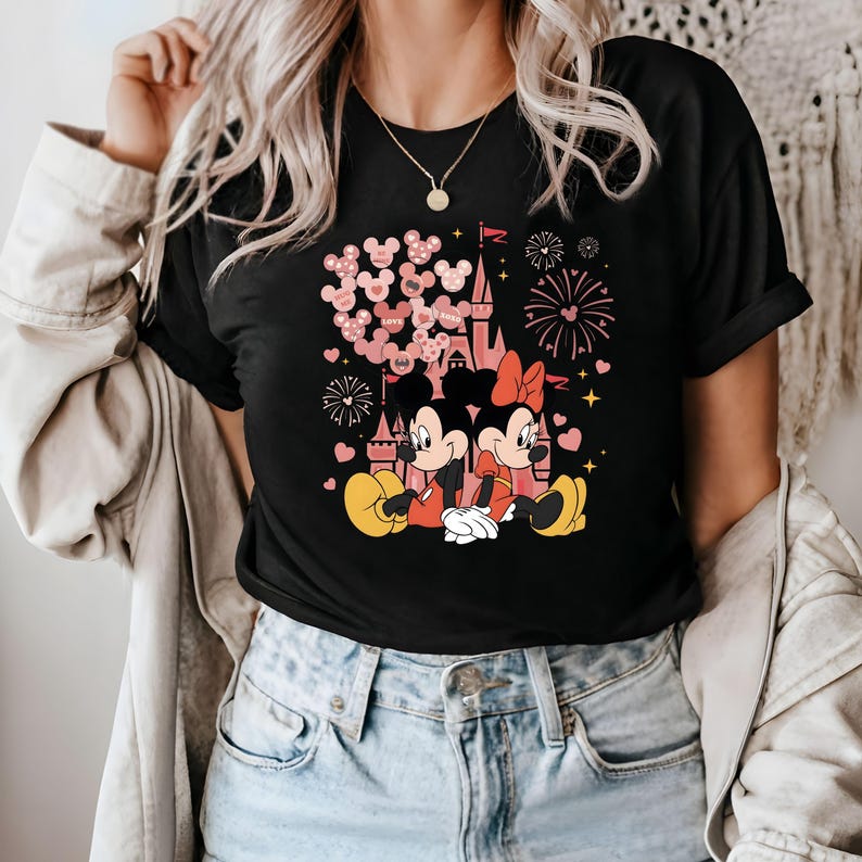 May include: Black t-shirt with a pink and red graphic of Mickey Mouse and Minnie Mouse in front of a pink castle with pink hearts and fireworks. The text "Save the Date" is visible on the graphic.