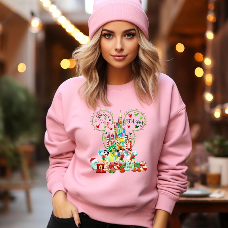 May include: Pink sweatshirt with a Mickey Mouse silhouette featuring the words "Mickey Very Merry Christmas" and a depiction of the Disney castle with various Disney characters.