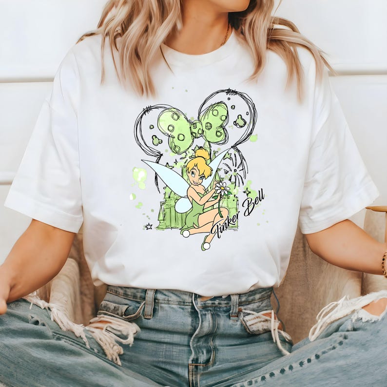 May include: White t-shirt with a green and black illustration of Tinker Bell with a flower and the text "Tinker Bell".
