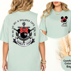 May include: A light green t-shirt with a Disney pirate theme. The back features an anchor design with a Minnie Mouse head, a red bow, and the text "YO HO HO A PIRATES LIFE FOR ME DISNEY 2026". The front has a pirate Mickey Mouse head.