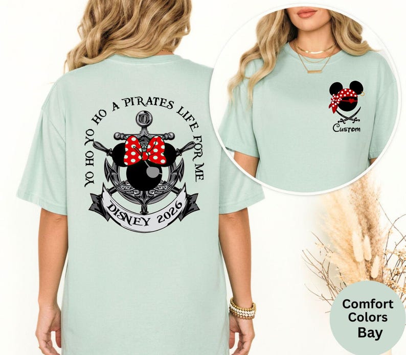 May include: A light green t-shirt with a Disney pirate theme. The back features an anchor design with a Minnie Mouse head, a red bow, and the text "YO HO HO A PIRATES LIFE FOR ME DISNEY 2026". The front has a pirate Mickey Mouse head.