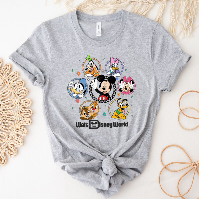 Op de afbeelding: Grijs T-shirt met een kleurrijke afbeelding van Mickey Mouse en andere Disney-figuren in cirkels. De tekst "Walt Disney World" staat onder de afbeelding.