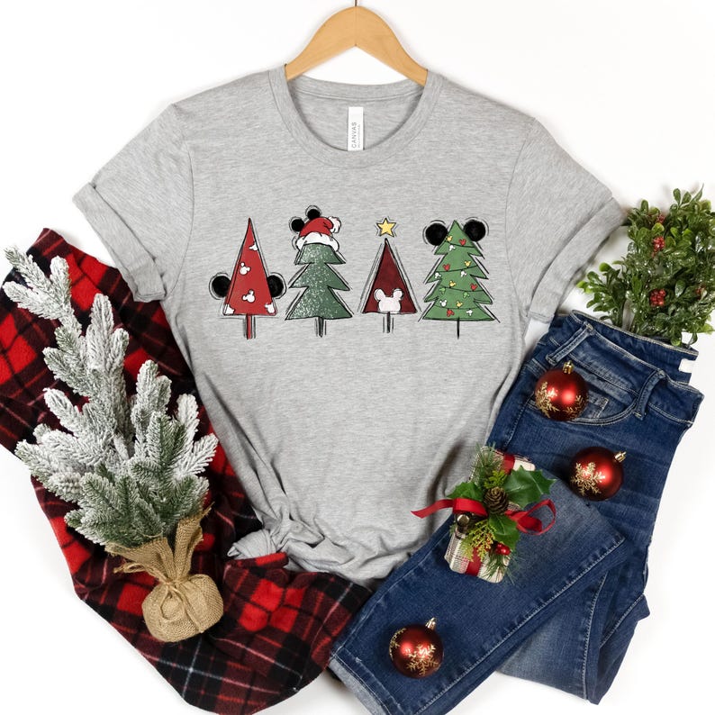 May include: A gray t-shirt with a Christmas tree design featuring Mickey Mouse ears and a Santa hat. The trees are decorated with red and green ornaments.