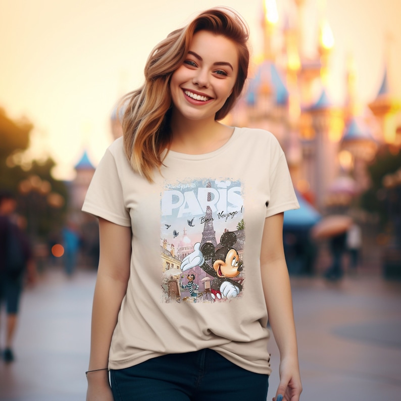 May include: A beige t-shirt with a graphic print of Mickey Mouse in front of the Eiffel Tower. The graphic also includes the text "Paris" and "Bien Voyage!"