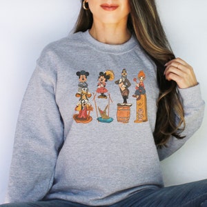 May include: A grey sweatshirt featuring a vintage cartoon print of Mickey Mouse, Minnie Mouse, Goofy, Donald Duck, and Pluto. The characters are arranged in a line and are wearing their signature outfits.