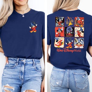 Puede incluir: Una camiseta azul marino con una ilustraci&oacute;n de Mickey Mouse roja y amarilla en el bolsillo delantero. La parte posterior de la camiseta presenta un collage de ilustraciones de Mickey Mouse en rojo, amarillo y azul con el texto "WALT DISNEY WORLD" en rojo.