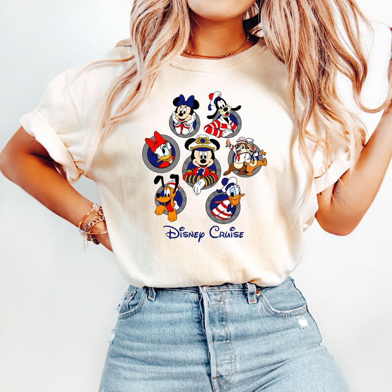May include: Cream-colored t-shirt featuring a colorful graphic of Disney characters in circular frames. The design includes Mickey Mouse, Minnie Mouse, Donald Duck, Goofy, Pluto, and Chip and Dale, with the text "Disney Cruise" below.