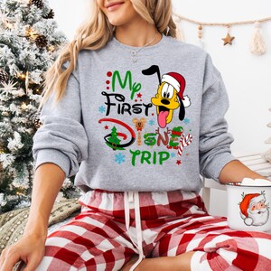 May include: A gray sweatshirt with a Christmas-themed design featuring Pluto wearing a Santa hat and the text "My First Disney Trip".