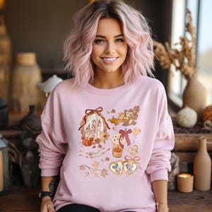 Puede incluir: Sudadera rosa claro con un dise&ntilde;o de tem&aacute;tica oto&ntilde;al. El dise&ntilde;o incluye un castillo, calabazas, Chip y Chop, y Mickey y Minnie Mouse en marcos con forma de coraz&oacute;n. La sudadera tiene mangas largas y cuello redondo.