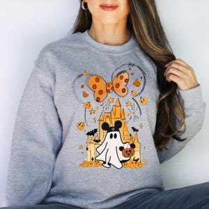 May include: A gray sweatshirt with a Halloween-themed design featuring a ghost holding a pumpkin, a castle, and a bow. The design is in orange and black.