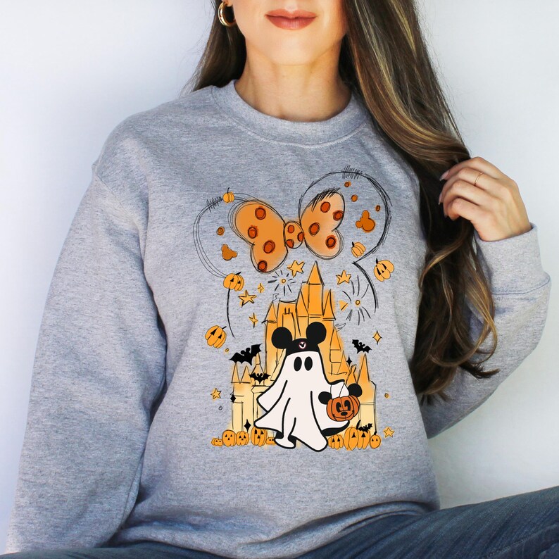 May include: A gray sweatshirt with a Halloween-themed design featuring a ghost holding a pumpkin, a castle, and a bow. The design is in orange and black.