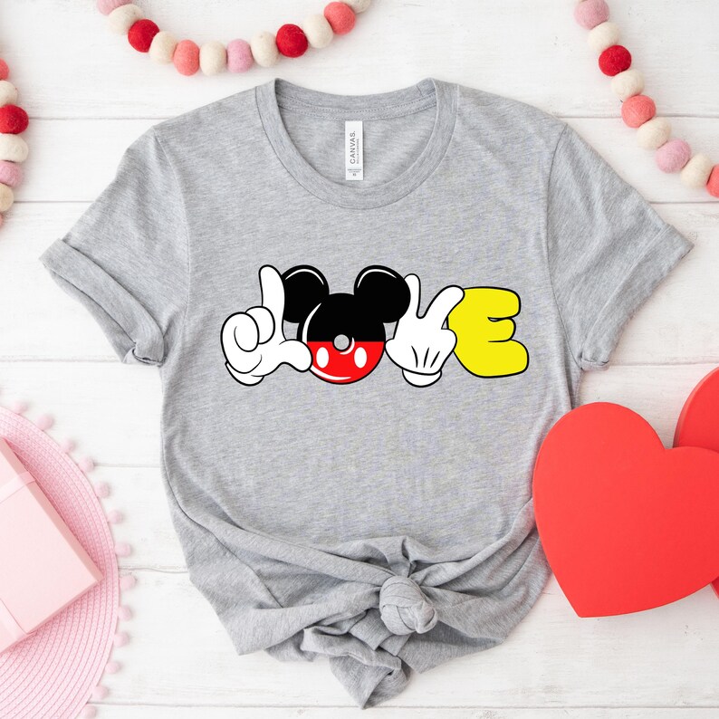 May include: Gray t-shirt with a Mickey Mouse design that spells out "LOVE" in sign language. The Mickey Mouse head is red and black with yellow gloves.