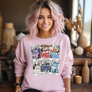 May include: A pink sweatshirt with a graphic print of the Cars characters dressed up for Halloween. The characters are Mater, McQueen, Sally, Luigi, Doc Hudson, and Guido. The text "Halloween" is printed above the characters.