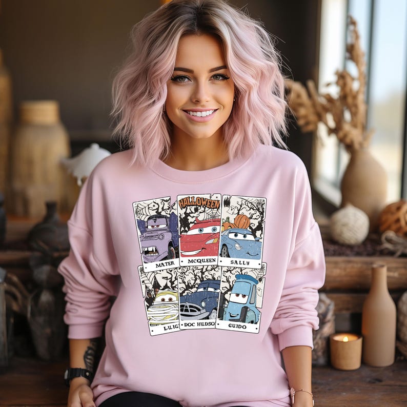 May include: A pink sweatshirt with a graphic print of the Cars characters dressed up for Halloween. The characters are Mater, McQueen, Sally, Luigi, Doc Hudson, and Guido. The text "Halloween" is printed above the characters.