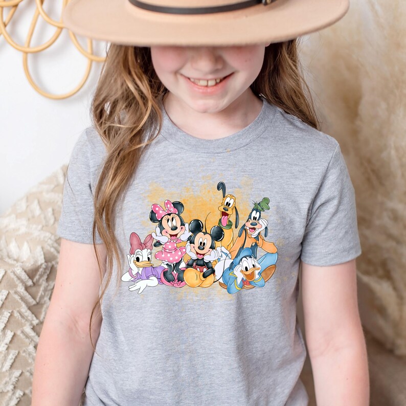 Puede incluir: Una camiseta gris con un estampado gr&aacute;fico colorido de Mickey Mouse, Minnie Mouse, Donald Duck, Goofy y Pluto. Los personajes sonr&iacute;en y parecen estar divirti&eacute;ndose juntos.