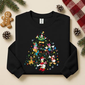 K&ouml;nnte beinhalten: Schwarzes Sweatshirt mit Rundhalsausschnitt und einem Weihnachtsbaumdesign mit Disney-Figuren. Der Baum ist mit bunten Lichtern, Kugeln und Sternen geschm&uuml;ckt. Micky Maus, Minnie Maus, Donald Duck und Goofy geh&ouml;ren zu den Figuren.