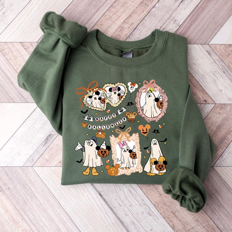 May include: Green sweatshirt featuring a Halloween-themed graphic. The design includes cartoon ghosts, pumpkins, bats, and the text "Happy Halloween." The graphic is in a variety of colors, including white, orange, and black.