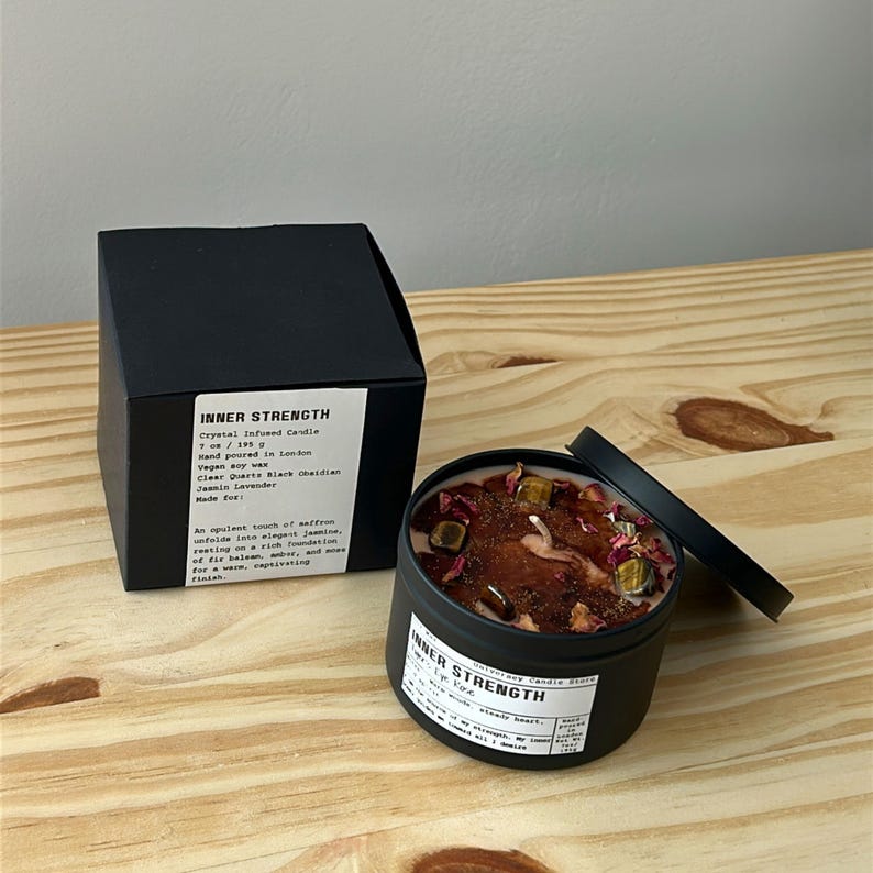 May include: A black candle tin and matching box labeled Inner Strength, containing vegan soy wax, crystal-infused with clear quartz, black obsidian, and tiger's eye, topped with dried flower petals. The label specifies 7 oz / 195 g net weight.