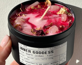 Può includere: Una candela in barattolo di metallo nero con un'etichetta bianca che riporta la scritta INNER GODDESS, Rose Quartz Jasmine Rose. La superficie in cera di soia è rosa e rossa, decorata con cristalli di quarzo rosa e petali di rosa.