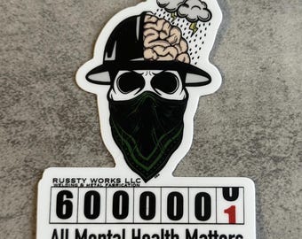 May include: A white sticker featuring a skull wearing a black hat and bandana, with a brain exposed. Above the skull are storm clouds and rain. The sticker includes the text "600001" and "All Mental Health Matters."