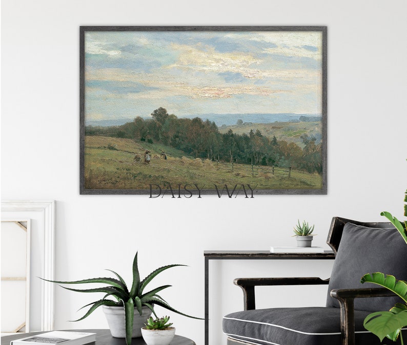 May include: A framed landscape painting depicting a rural scene with a field, trees, and a cloudy sky. The painting is in a gray frame and is hanging on a white wall.