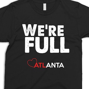 May include: Black t-shirt with white text that reads "We're Full Atlanta" with a red heart.