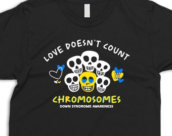 Puede incluir: Camiseta negra con un gráfico de calaveras amarillas y azules con el texto "Love Doesn't Count Chromosomes Down Syndrome Awareness".
