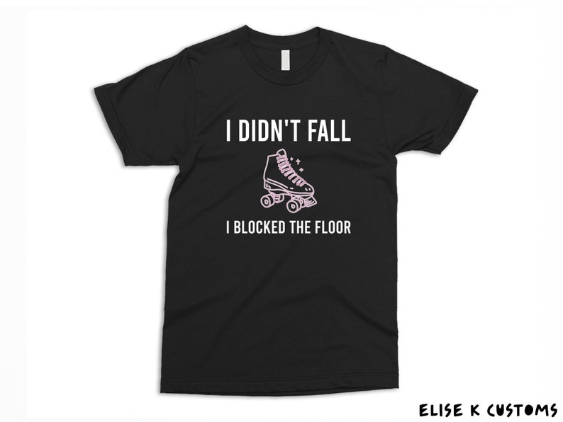 K&ouml;nnte beinhalten: Schwarzes T-Shirt mit wei&szlig;em Text, der "Ich bin nicht gefallen, ich habe den Boden blockiert" lautet. Eine rosa Rollschuhgrafik befindet sich &uuml;ber dem Text.