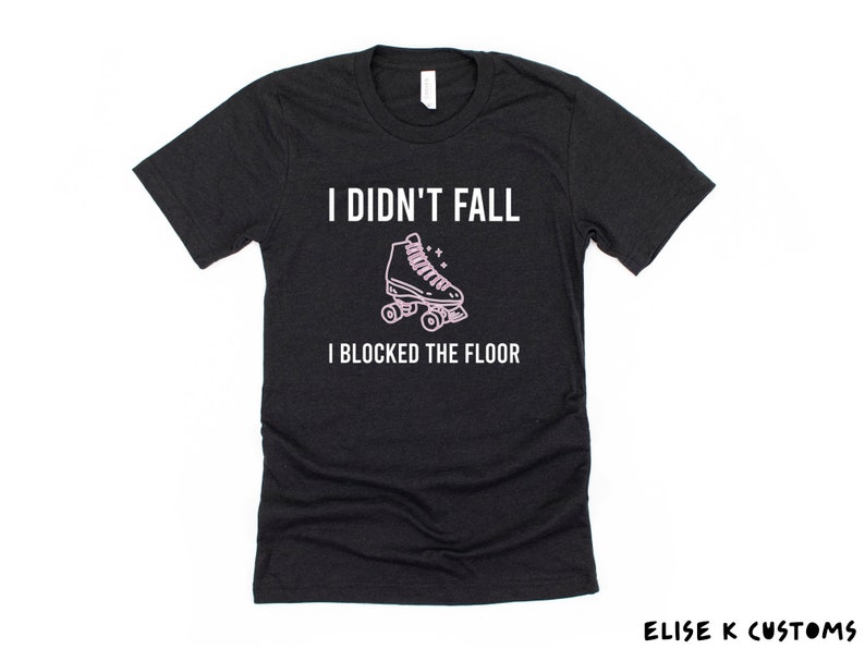K&ouml;nnte beinhalten: Schwarzes T-Shirt mit dem Text "Ich bin nicht gefallen, ich habe den Boden blockiert" in Wei&szlig;. Eine rosa Rollschuhgrafik befindet sich &uuml;ber dem Text.