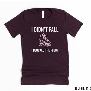 K&ouml;nnte beinhalten: Ein dunkelviolettes T-Shirt mit dem Text "Ich bin nicht gefallen, ich habe den Boden blockiert" und einer rosa Umrandung einer Rollschuh.