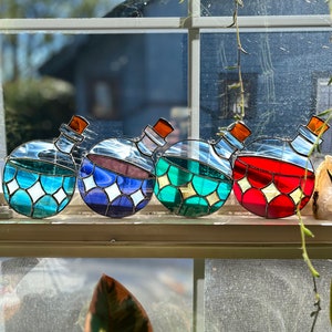 May include: Four stained glass potion bottles in different colors: blue, purple, green, and red. Each bottle has a cork stopper and a gold rim.
