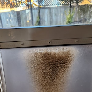 May include: A close-up of a white pet door with a brown stain on the glass. The text "REPLACEMENT FLAP/PATCH FLAP" is printed on the glass.