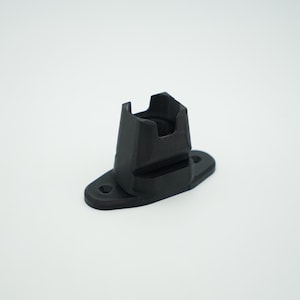 May include: A black plastic mount with a rectangular opening for attaching a device. The mount has a flat base with a small hole in the center.