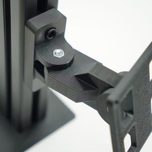 May include: A black 3D printed bracket with a silver screw and nut. The bracket is attached to a black metal pole and has a flat surface on the other side.
