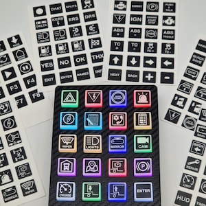 May include: A black control panel with illuminated square buttons and various sticker sheets. The buttons display icons and text like "Lights," "Mirror," and "Enter." The stickers feature labels such as "Fuel," "ABS," and "Chat."