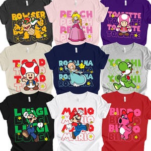 May include: Nine colorful t-shirts featuring characters from a video game. The shirts display characters like Bowser, Peach, Toadette, Toad, Rosalina, Yoshi, Luigi, Mario, and Birdo, with their names printed in bold text.
