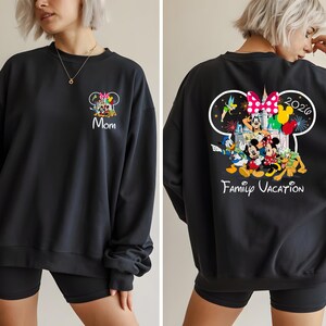 May include: Black sweatshirt featuring a colorful Disney family graphic on the front and back. The front displays "Mom" and the back shows "Family Vacation 2020" with Mickey, Minnie, Donald, and other characters. A comfortable, casual style.