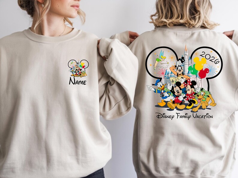 May include: Beige sweatshirt featuring Disney characters. The front has a Mickey Mouse head design with characters and the word "Name". The back displays a larger Mickey Mouse head design with characters, fireworks, the year "2020", and "Disney Family Vacation".