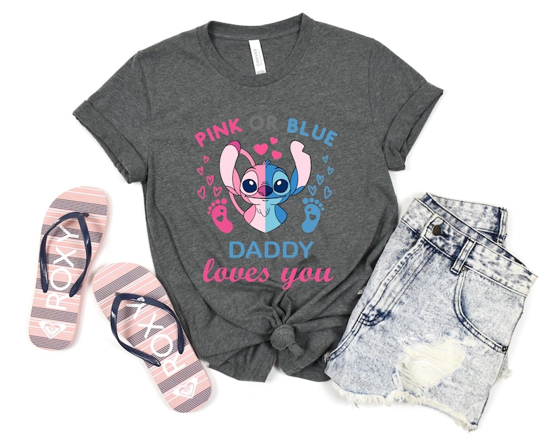 Puede incluir: Una camiseta gris con un gr&aacute;fico de Stitch rosa y azul. El texto "Pink or Blue Daddy loves you" est&aacute; impreso en la camiseta.