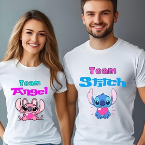 Puede incluir: Dos camisetas blancas con un personaje de dibujos animados Stitch. Una camiseta dice "Team Angel" con un Stitch rosa sosteniendo un coraz&oacute;n. La otra camiseta dice "Team Stitch" con un Stitch azul sosteniendo un coraz&oacute;n.