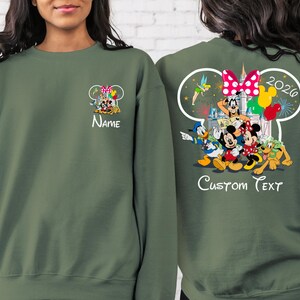 May include: Olive green sweatshirt featuring Disney characters Mickey, Minnie, Donald, Goofy, and Pluto. The front has a small graphic with the word "Name". The back has a larger graphic with "2026" and "Custom Text".