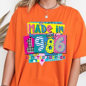 May include: Orange t-shirt with the text "MADE IN 1986 LIMITED EDITION" in a colorful, retro design. The design includes the numbers 1, 9, 8, and 6, with a cassette tape graphic.