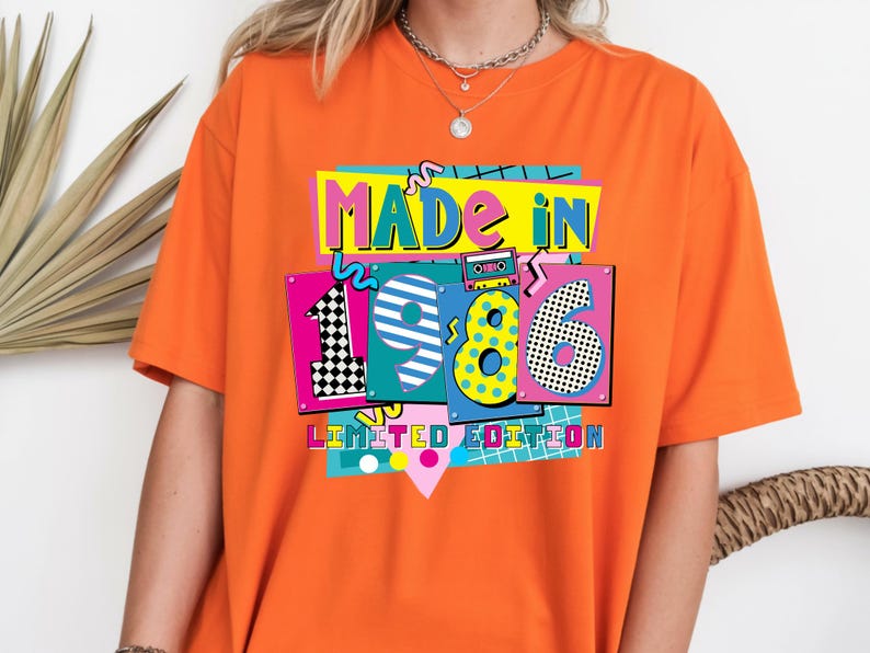 May include: Orange t-shirt with the text "MADE IN 1986 LIMITED EDITION" in a colorful, retro design. The design includes the numbers 1, 9, 8, and 6, with a cassette tape graphic.
