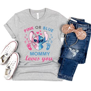 Puede incluir: Camiseta gris con un personaje Stitch azul y rosa sosteniendo un pie de beb&eacute; rosa y azul. El texto "Pink or Blue Mommy loves you" est&aacute; impreso en la camiseta.