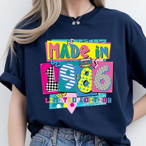 May include: Navy blue t-shirt with a colorful graphic that reads "MADE IN 1986 LIMITED EDITION." The design features vibrant colors and a retro aesthetic, with the numbers 1, 9, and 6 in a playful font.