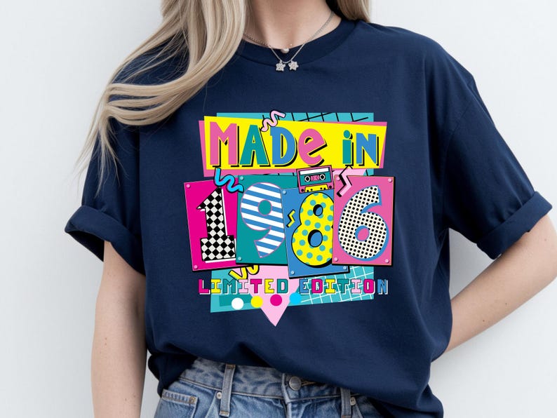 May include: Navy blue t-shirt with a colorful graphic that reads "MADE IN 1986 LIMITED EDITION." The design features vibrant colors and a retro aesthetic, with the numbers 1, 9, and 6 in a playful font.