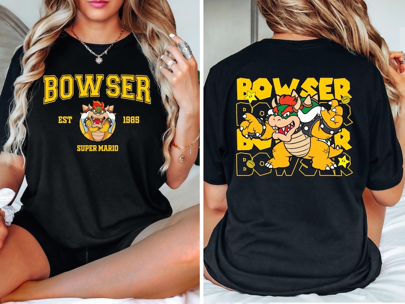 May include: Black t-shirt featuring a yellow and orange Bowser graphic from Super Mario. The front design includes the word "BOWSER" above a cartoon image of Bowser, with "EST 1985" and "SUPER MARIO" below. The back of the shirt repeats the "BOWSER" text.